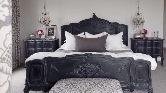 Black double bed with carved foot, matching bedside cabinets and ottoman with pale brocade cover